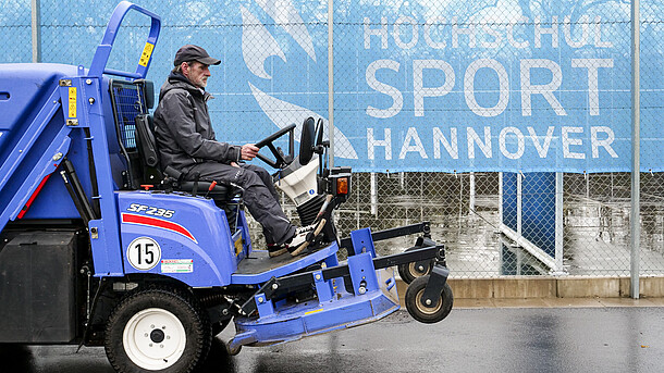 ein technischer Mitarbeiter sitzt auf einer Säuberungsmaschine und fährt über den SportCAMPUS